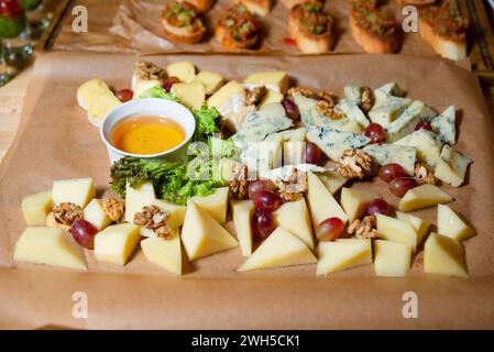 Eine appetitliche Käseplatte mit einer Vielzahl von Gourmet-Käsesorten, begleitet von frischen Trauben, Walnüssen und einer Schüssel Honig auf Pergament Stockfoto