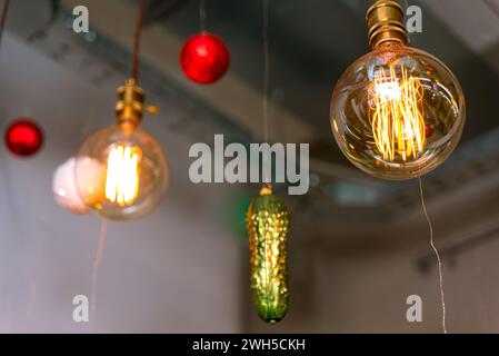 Ein sanfter Blick auf Edison-Glühbirnen, die warm neben unscharfen Weihnachtskugeln leuchten und moderne und traditionelle Feiertagselemente miteinander verbinden. Stockfoto