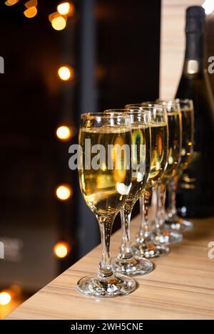 Reihe von Sektgläsern gefüllt mit Sekt, bereit für eine Feier, mit warmen Bokeh-Lichtern, die sanft im Hintergrund leuchten. Stockfoto