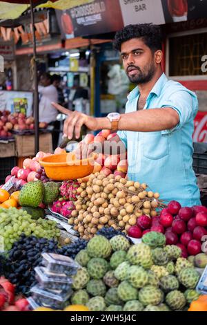 Ein junger Indianer verkauft Obst in seinem Laden auf einem lokalen Markt Goa India. Mann, der Gemüse und Obst an Kunden auf einem Markt auf dem Goa Bazar verkauft. Stre Stockfoto