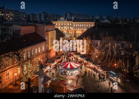 Budapest, Ungarn - aus der Vogelperspektive auf den Weihnachtsmarkt und das Karussell auf dem Szentlelek-Platz, Obuda in der Abenddämmerung. Dekorative beleuchtete Geschäfte, festliche Dekorationen Stockfoto