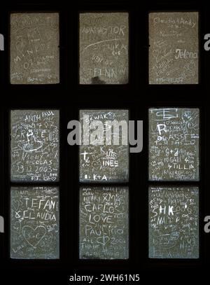 Ein vertikaler Schuss von Namen und Herzen, die in schmutzige alte Fensterscheiben eingeritzt sind Stockfoto