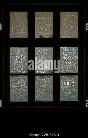 Ein vertikaler Schuss von Namen und Herzen, die in schmutzige alte Fensterscheiben eingeritzt sind Stockfoto