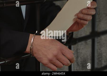 Ein Mann in einem Anzug mit Handschellen am Handgelenk, der ein Stück Papier hält, Zellstangen. Stockfoto