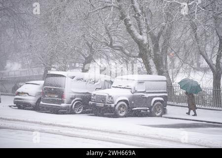 Eine Person läuft an schneebedeckten Autos in Buxton, Peak District, vorbei. In Teilen Englands und Wales werden bis zu 25 cm Schnee prognostiziert, da das Met Office Wetterwarnungen ausgab und vor Reisestörungen warnte. Bilddatum: Donnerstag, 8. Februar 2024. Stockfoto