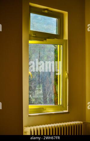 Ein warmer und gemütlicher Blick durch das gelbe Fenster im Inneren, wo das Sonnenlicht den Raum in ein lebendiges Licht taucht. Stockfoto