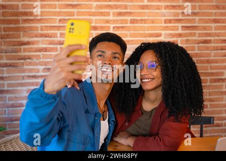 Ein paar Frauen und Männer verschiedener Nationalitäten nehmen Selfies mit ihrem Telefon und lächeln drinnen Stockfoto