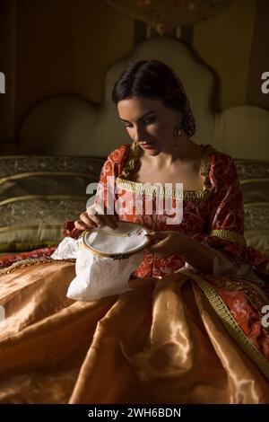 Golden mittelalterliches Schlafzimmer mit wunderschönem Himmelbett. Eine Dame im Renaissance-Kleid, die stickt. Stockfoto