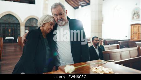 Beerdigung, Sarg und Seniorenpaar umarmen sich in der Kirche für Abschied, Trauer und Trauer im Gedenkgottesdienst. Depression, traurige Familie und Mann umarmen Frau durch Stockfoto