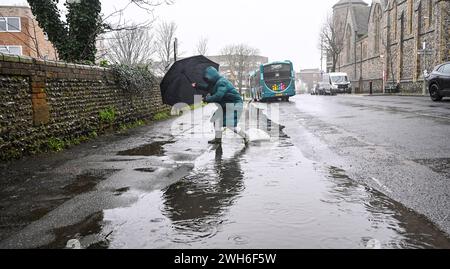 Brighton Großbritannien 8. Februar 2024 - Eine Frau springt bei starkem Regen in Brighton über eine große Pfütze an dem Tag, an dem bekannt gegeben wurde, dass die globalen Temperaturen um mehr gestiegen sind und das 1,5C-Ziel 2023 verfehlt wurde: Credit Simon Dack / Alamy Live News Stockfoto