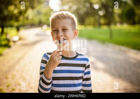 Porträt eines glücklichen Jungen, der im Park steht und Eis isst. Stockfoto