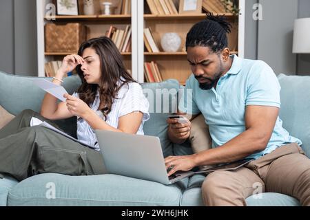 Fokussierte besorgt paar Rechnungen bezahlen online auf Laptop mit Dokumenten sitzen zusammen auf dem Sofa zu Hause, ernsthaft verwirrt Mann und Frau Planung Haushalt e Stockfoto