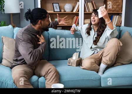 Unglückliche junge Frau, die auf dem Sofa sitzt und einen Schwangerschaftstest hat, ein afroamerikanischer Ehemann, der sie anschrie, drinnen. Millennial Familie hat Konflikt über un Stockfoto