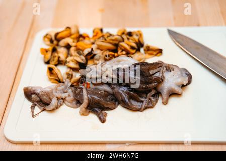 Frische Meeresfrüchte-Auswahl mit Tintenfisch und Muscheln, zubereitet auf einem weißen Schneidebrett, bereit für das Kochen einer köstlichen Mahlzeit. Stockfoto