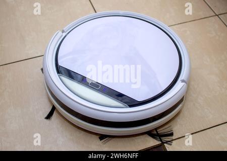 Roboter-Staubsauger, der in der Küche arbeitet und Schmutz vom Fliesenboden fegt Stockfoto