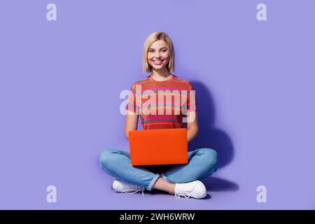 Ganzkörperfoto des charmanten Mädchens tragen trendiges Outfit mit Netbook-Browsing in sozialen Medien, um Angebote isoliert auf lila Hintergrund zu finden Stockfoto