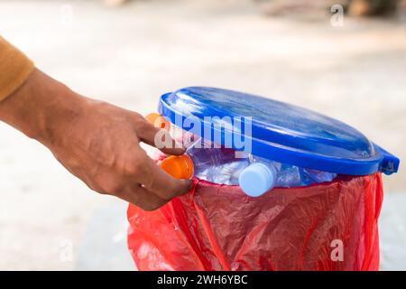 Eine männliche Hand, die eine leere Plastikwasserflasche in den Recyclingbehälter wirft Stockfoto