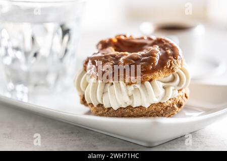 Veternik: Süßer Donut, typisch slowakischer süßer Kuchen mit Sahnefüllung, garniert mit Karamell auf einem Teller in einem Café. Stockfoto