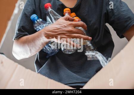 Ein Mann sammelt und legt recycelbare Plastikflaschen in einen Karton Stockfoto