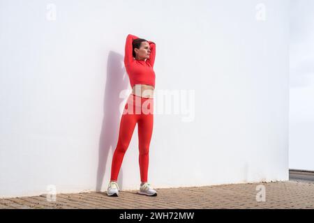 Sportliche Frau, die eine Arm-Dehnübung macht, draußen, weiße Wand. Stockfoto