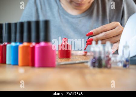 Frau, die zu Hause ihre Nägel malt, mit einer knallroten Farbe. Stockfoto