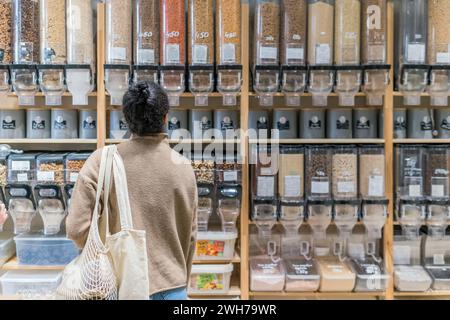 Junge Afroamerikanerin mit Öko-Taschen in einem Zero Waste Supermarkt. Rückansicht einer Afroamerikanerin, die Getreide und Getreide kauft Stockfoto