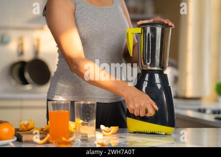 Nahaufnahme einer Frau, die Orange mit Mixer Entsafter in aktiver Kleidung am Morgen zubereitet - Konzept von Fitness-Lifestyle, Entgiftung und hausgemachtem Saft Stockfoto