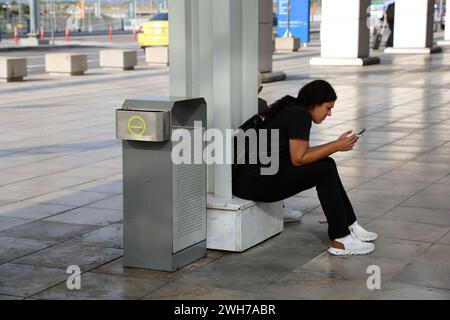 Athen Griechenland internationaler Flughafen Athen (AIA) Eleftherios Venizelos Frau, die in der Nähe von bin sitzt, mit Handy Stockfoto