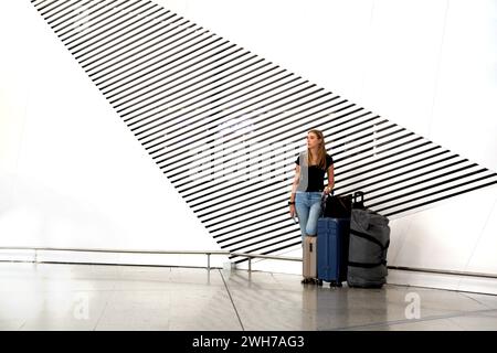 Athen Griechenland internationaler Flughafen Athen (AIA) Eleftherios Venizelos Frau mit Koffern neben künstlerischen Lüftungsschlitzen in der Mauer Stockfoto