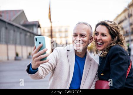 Glückliches Touristenpaar im mittleren Erwachsenenalter, das zusammen reist und ein Selfie mit ihrem Gepäck macht. Liebevoller älterer Ehemann und Ehefrau, die während eines Fotos machen Stockfoto