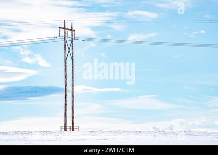 Isolierter Strommast auf einem schneebedeckten Präriefeld mit Freileitungen und Kabeln in den kanadischen Prärien im Rocky View County Alberta. Stockfoto