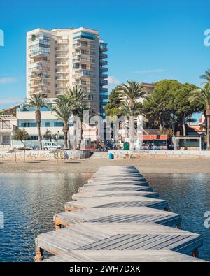 Eine hölzerne Promenade an einem Sandstrand führt zu einem palmengesäumten Hotel Stockfoto
