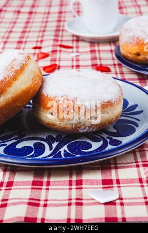 Das Bild zeigt zwei stimulierende Donuts auf einem Teller. Die Donuts sind mit einer Schicht Puderzucker bedeckt und haben eine runde, pralle Form. Stockfoto