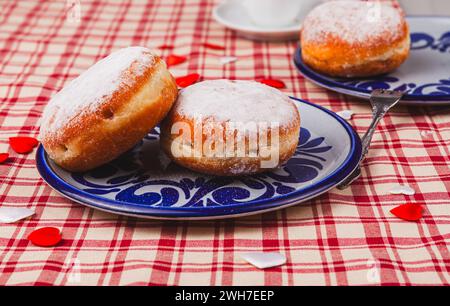 Das Bild zeigt zwei stimulierende Donuts auf einem Teller. Die Donuts sind mit einer Schicht Puderzucker bedeckt und haben eine runde, pralle Form. Stockfoto