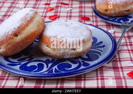 Das Bild zeigt zwei stimulierende Donuts auf einem Teller. Die Donuts sind mit einer Schicht Puderzucker bedeckt und haben eine runde, pralle Form. Stockfoto