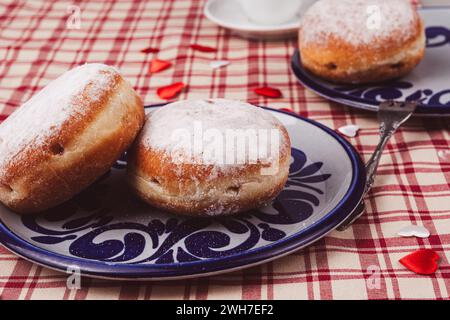 Das Bild zeigt zwei stimulierende Donuts auf einem Teller. Die Donuts sind mit einer Schicht Puderzucker bedeckt und haben eine runde, pralle Form. Stockfoto