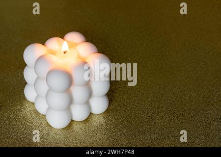 Kerze mit Bubble Cube-Duft auf goldenem Hintergrund mit Kopierraum. Kerzenlicht sorgt für warme, entspannte Stimmung. Stockfoto