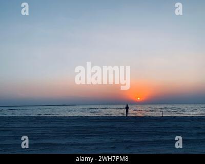 Eine Person, die am Strand steht und bei Sonnenuntergang auf das Meer blickt Stockfoto
