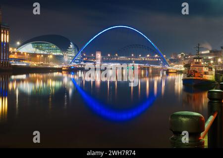 Newcastle Kai und Tyne Brücken bei Nacht mit Lichtreflexen im Fluss Tyne. Ein Boot liegt am Kai an und das Glass House ist auf der. Stockfoto