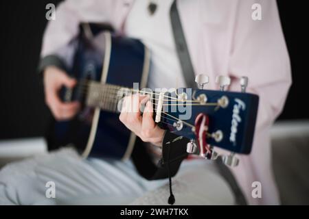 Ein junger schlanker attraktiver Mann in weißem Hemd, der blaue Gitarre auf schwarzem Hintergrund spielt, Nahaufnahme Stockfoto