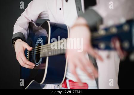 Ein junger schlanker attraktiver Mann in weißem Hemd, der blaue Gitarre auf schwarzem Hintergrund spielt, Nahaufnahme Stockfoto