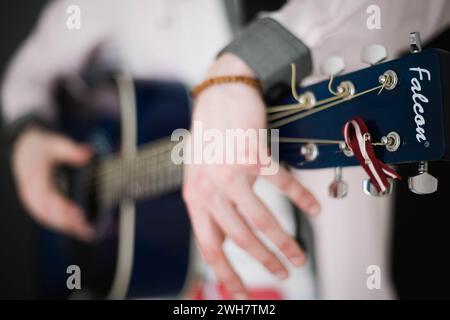 Ein junger schlanker attraktiver Mann in weißem Hemd, der blaue Gitarre auf schwarzem Hintergrund spielt, Nahaufnahme Stockfoto