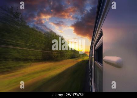 Personenzug in Bewegung mit Unschärfeeffekt im Wald bei Sonnenuntergang. Ansicht vom Zugfenster. Stockfoto