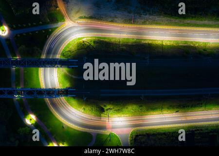 Die Straße biegt um die Eisenbahnbrücke. Nachtaufnahme mit langer Belichtung. Stadtlandschaft aus der Vogelperspektive. Stockfoto