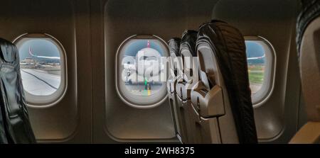 Blick von einem Flugzeug durch die Kabinenfenster auf ein anderes Flugzeug in Frontalansicht während des Tages Stockfoto