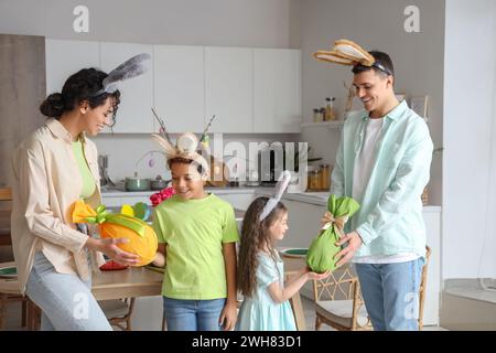 Glückliche Eltern geben ihren kleinen Kindern am Ostertag in der Küche Eier Stockfoto