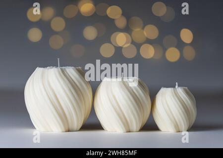 Drei handgefertigte Kerzen aus Sojabach unterschiedlicher Größe auf weißem Tisch mit grauem Hintergrund, Bokeh und Kopierraum. Kerzenherstellung, Bastelkonzept. Stockfoto