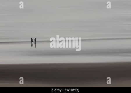 Zwei Personen gehen allein am Strand am Westufer von Llandudno entlang und nutzen den Adamski-Effekt, um den Hintergrund zu verwischen Stockfoto