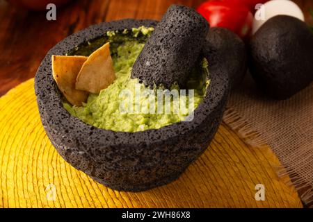 Guacamol. Avocado-Dip mit Tortilla-Chips, auch Nachos genannt, serviert in einer Schüssel aus vulkanischem Steinmörtel und Pistill, bekannt als Molcajete. Mexikanisch Stockfoto