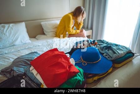 Flugstornierung. Verärgerte Frau, die mit Koffern mit Kleidung auf dem Bett sitzt. Stockfoto